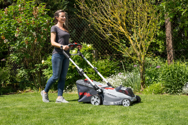 Frau benutzt den IKRA BOSCH Akku-Rasenmäher IB-LM 43 auf einem gepflegten grünen Rasen in einem Garten.
