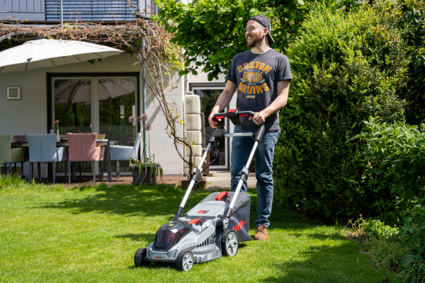 Mann mäht Rasen mit Akku Rasenmäher IKRA IB-LM 43 BOSCH 36V vor Einfamilienhaus.