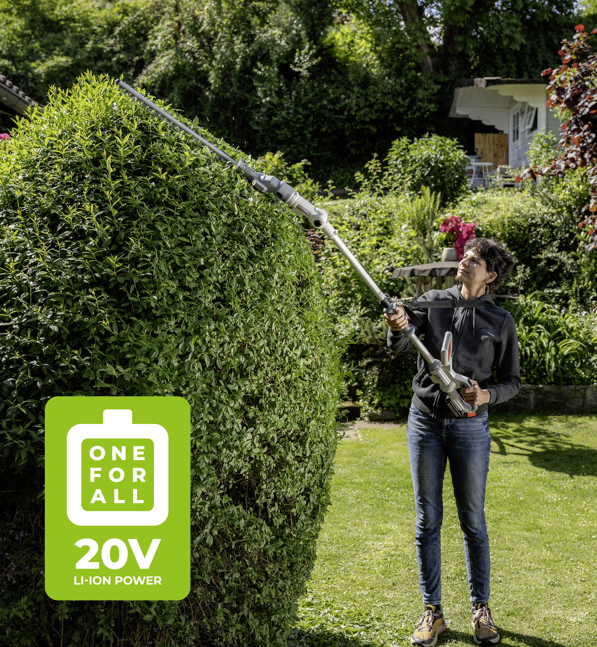 eine Frau schneidet mit einer IKRA Teleskop Heckenschere einen hohen Busch im Garten