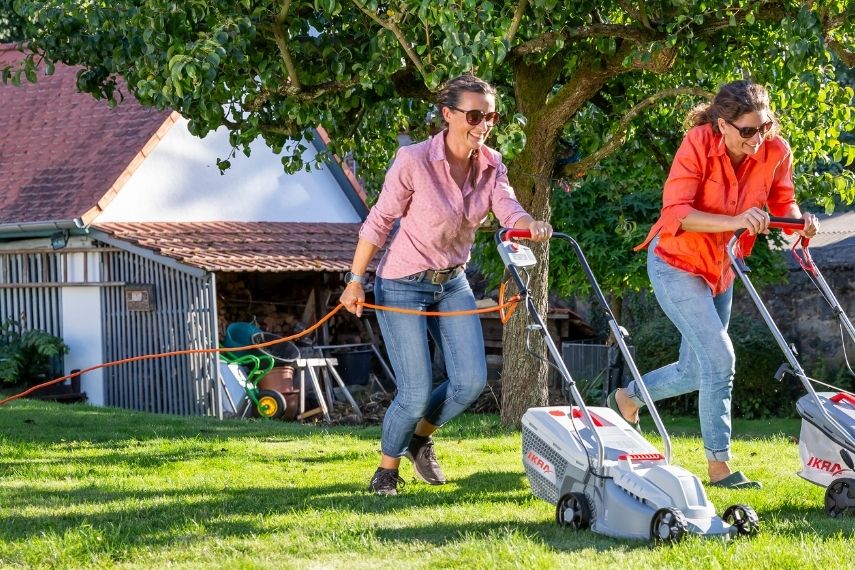 Zwei Frauen Rennen mit Rasenmähern um die Wette.