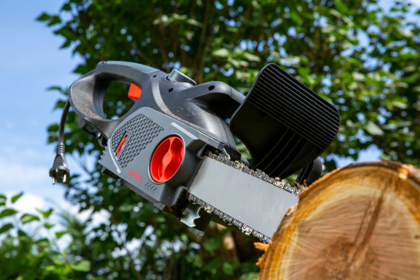 Elektro Kettensäge KSE 2400-40 mit eingestecktem Schwert im Baumstamm – Detailaufnahme vor bewaldetem Hintergrund.