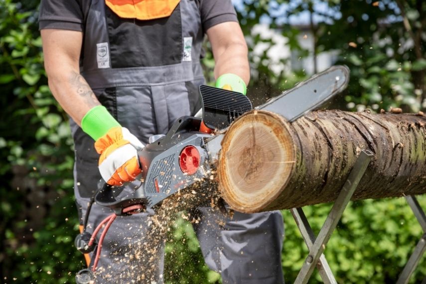 Eine Nahaufnahme zeigt, wie die Elektro Kettensäge KSE 2400-40 bei der Arbeit an einem Holzbalken fest mit zwei Händen geführt wird.