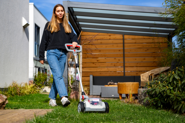 Junge Frau mäht im Garten mit dem kompakten Akku-Einhandmäher ICHM 20 von IKRA. Sie führt das Gerät mit einer Hand über eine Rasenfläche.