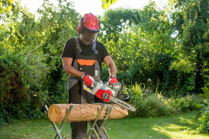 Ein Mann mit Schutzkleidung arbeitet mit der Akku Kettensäge ICC 2/2035 an einem Holzstamm, der auf einem Sägebock liegt.