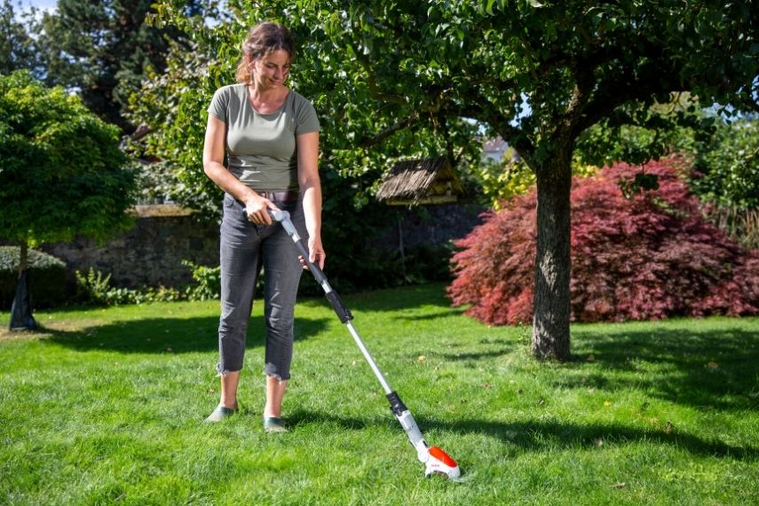 Eine Frau arbeitet rückenschonend mit der Gras- und Strauchschere IGBS 1210 F mit Fahrstock.